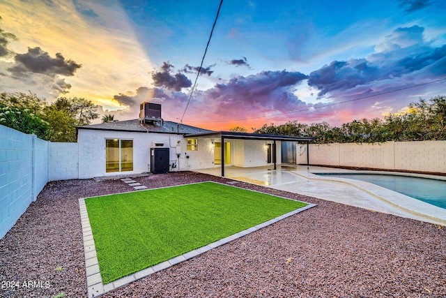 back house at dusk featuring a patio area, a fenced in pool, and central air condition unit