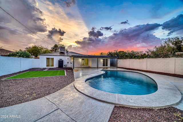 pool at dusk with a patio area and a yard