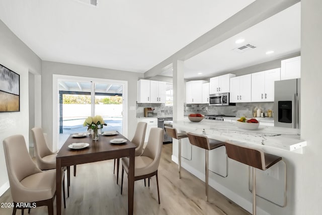 kitchen with light stone countertops, appliances with stainless steel finishes, decorative backsplash, a kitchen breakfast bar, and white cabinetry