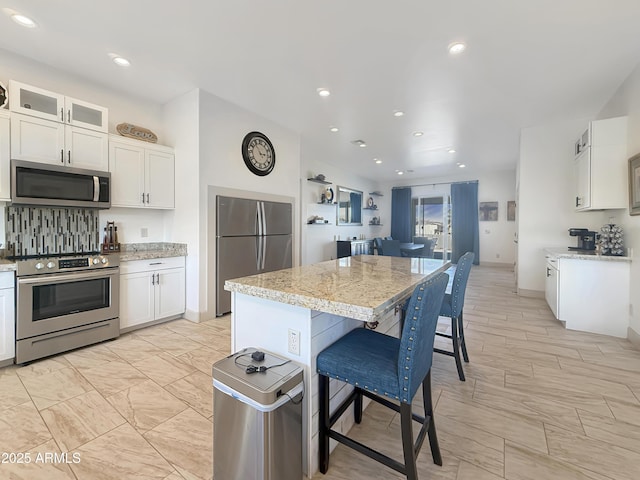 kitchen with white cabinetry, stainless steel appliances, a center island, a kitchen breakfast bar, and light stone counters