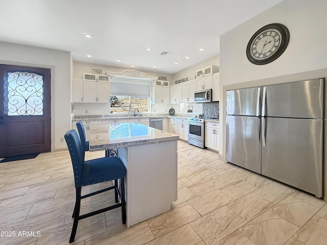 kitchen featuring white cabinetry, light stone counters, a center island, and appliances with stainless steel finishes