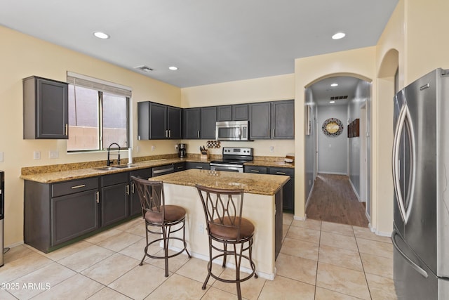 kitchen featuring sink, stainless steel appliances, light stone countertops, and a center island