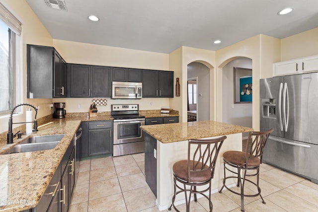 kitchen with appliances with stainless steel finishes, light stone countertops, light tile patterned floors, a kitchen island, and sink