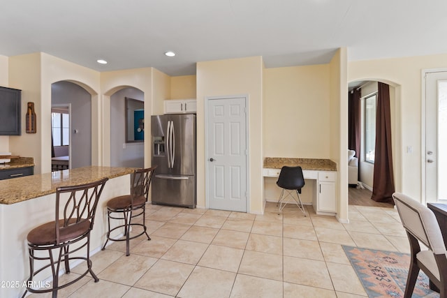 kitchen featuring built in desk, stainless steel fridge, a breakfast bar, light stone counters, and white cabinetry