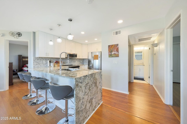 kitchen with stainless steel appliances, hanging light fixtures, decorative backsplash, white cabinets, and a peninsula