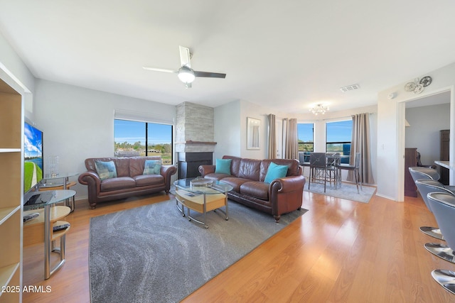 living room featuring light wood-style floors, visible vents, a fireplace, and ceiling fan