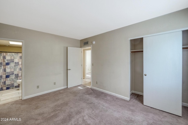 unfurnished bedroom with a closet, light colored carpet, and ensuite bathroom