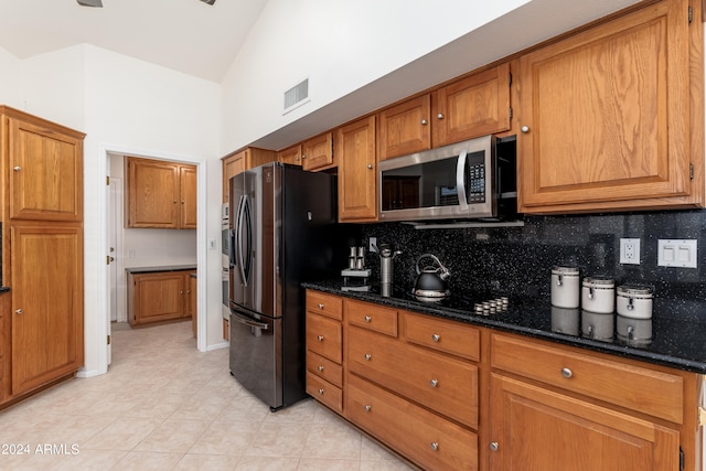 kitchen featuring high vaulted ceiling, stainless steel appliances, decorative backsplash, and dark stone counters