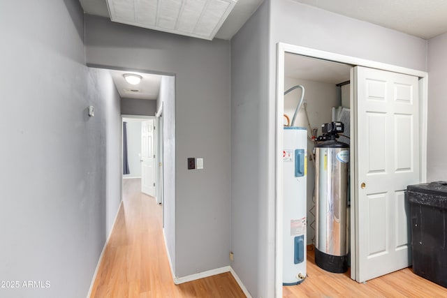 hall with baseboards, electric water heater, visible vents, and light wood finished floors