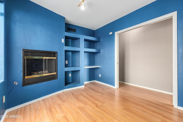 unfurnished living room featuring built in features, visible vents, a glass covered fireplace, wood finished floors, and baseboards