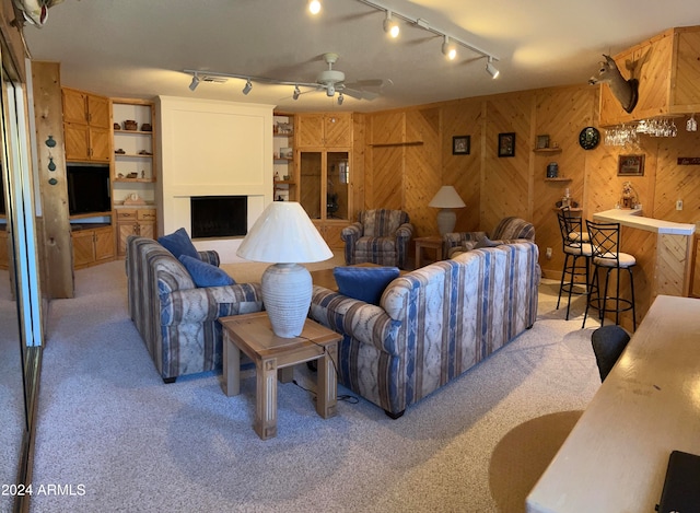 living room featuring light carpet, wood walls, rail lighting, and ceiling fan