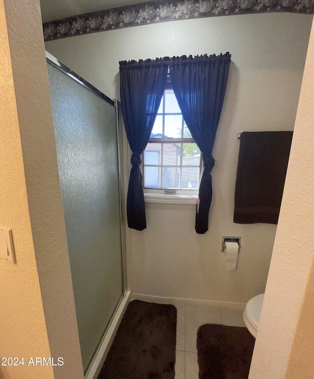 bathroom with a shower with door, toilet, and tile patterned flooring