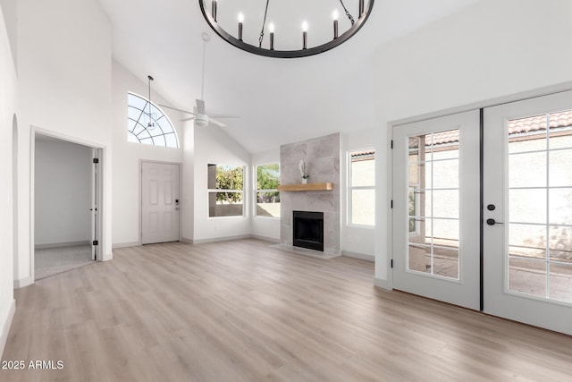 unfurnished living room with high vaulted ceiling, light wood finished floors, a tiled fireplace, and french doors