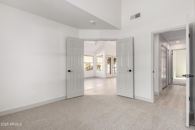 unfurnished bedroom featuring a towering ceiling, baseboards, visible vents, and light colored carpet