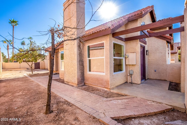 view of side of home with a fenced backyard, a tiled roof, a patio, and stucco siding