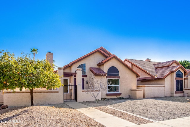 view of front of property featuring a fenced front yard, a tile roof, a chimney, stucco siding, and a gate