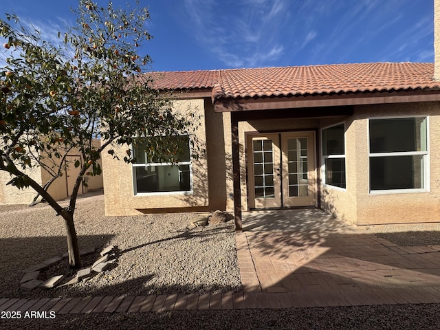 rear view of property with french doors, a tile roof, a patio, and stucco siding