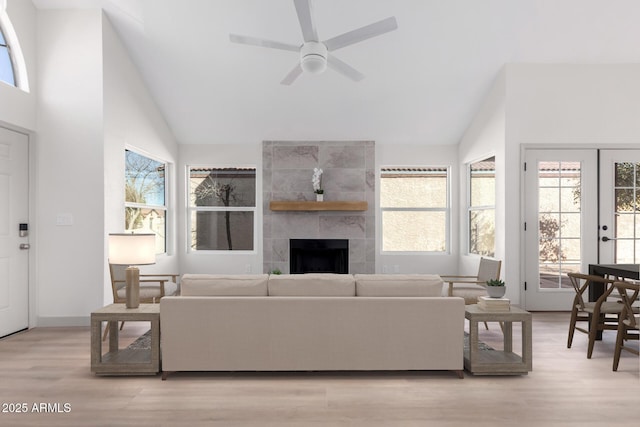 living area with high vaulted ceiling, a fireplace, a ceiling fan, light wood-style floors, and french doors