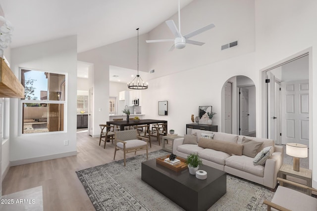 living area featuring light wood finished floors, visible vents, arched walkways, high vaulted ceiling, and ceiling fan with notable chandelier