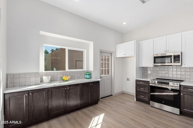 kitchen with dark brown cabinetry, white cabinetry, appliances with stainless steel finishes, light wood finished floors, and tasteful backsplash