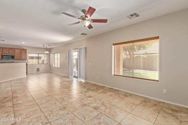 unfurnished living room with ceiling fan, a healthy amount of sunlight, and light tile patterned flooring