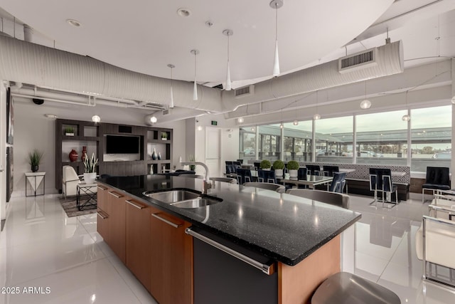 kitchen with dishwashing machine, sink, hanging light fixtures, light tile patterned flooring, and a large island with sink