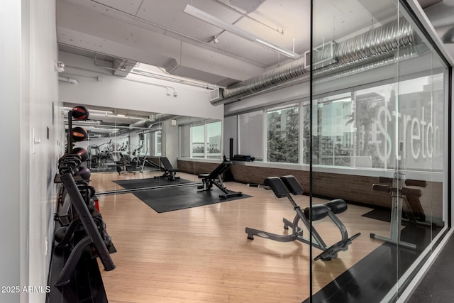 exercise room with hardwood / wood-style flooring and brick wall