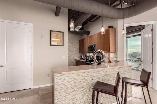 kitchen featuring a breakfast bar, appliances with stainless steel finishes, hanging light fixtures, light tile patterned flooring, and kitchen peninsula