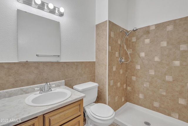 bathroom featuring tiled shower, vanity, toilet, and tile walls