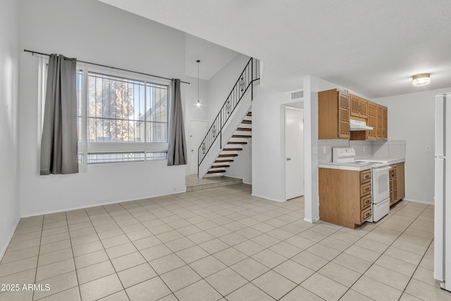 kitchen featuring under cabinet range hood, white appliances, light countertops, brown cabinets, and decorative backsplash