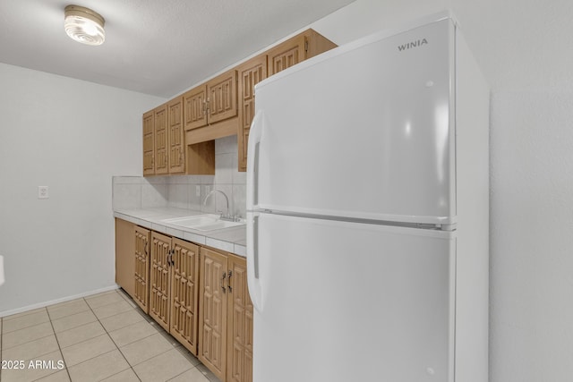 kitchen with light tile patterned floors, tasteful backsplash, tile countertops, freestanding refrigerator, and a sink