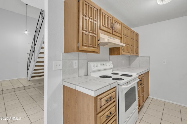 kitchen featuring light tile patterned floors, under cabinet range hood, backsplash, tile counters, and white electric range oven