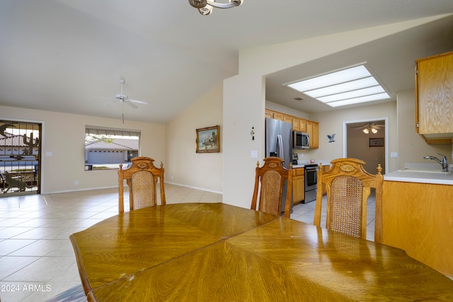 tiled dining area with ceiling fan, sink, and lofted ceiling with skylight