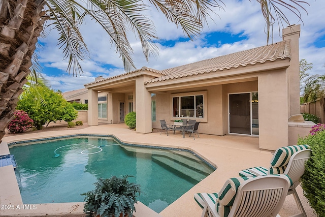 rear view of house featuring a fenced in pool, a tiled roof, fence, a patio area, and stucco siding