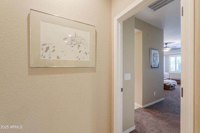 hallway with a textured wall, baseboards, visible vents, and carpet