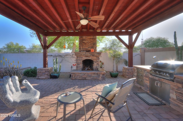 view of patio featuring grilling area, fence, an outdoor kitchen, and an outdoor stone fireplace