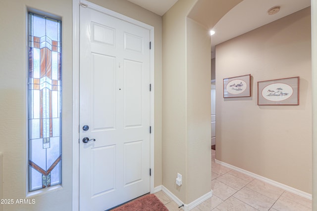foyer featuring arched walkways, baseboards, and light tile patterned floors