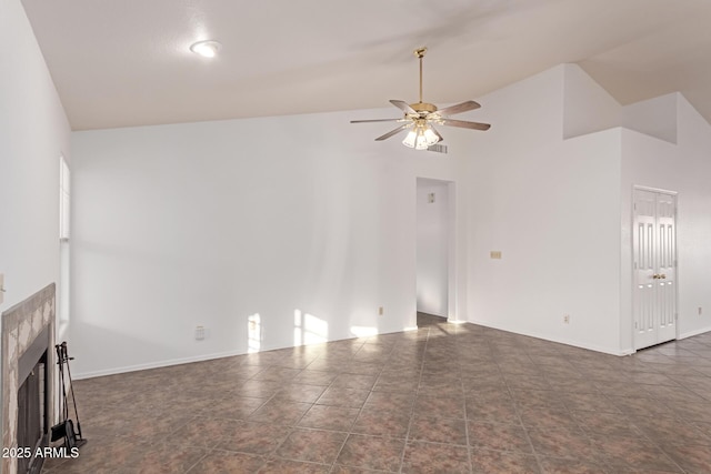 empty room featuring a tiled fireplace, lofted ceiling, dark tile patterned flooring, and ceiling fan