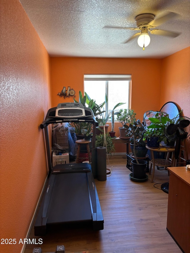 workout room featuring baseboards, a textured ceiling, wood finished floors, and a ceiling fan