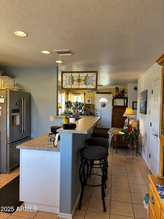 kitchen with visible vents, refrigerator with ice dispenser, a textured ceiling, light tile patterned flooring, and light countertops