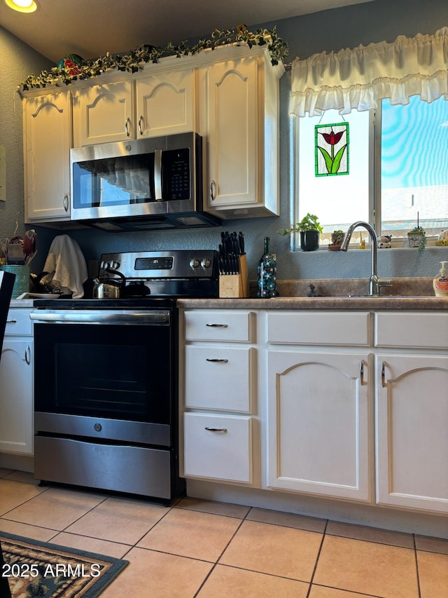 kitchen with dark countertops, light tile patterned flooring, white cabinets, stainless steel appliances, and a sink