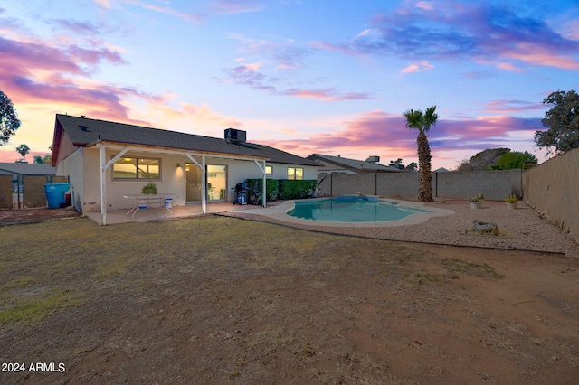 pool at dusk with a yard, cooling unit, and a patio area