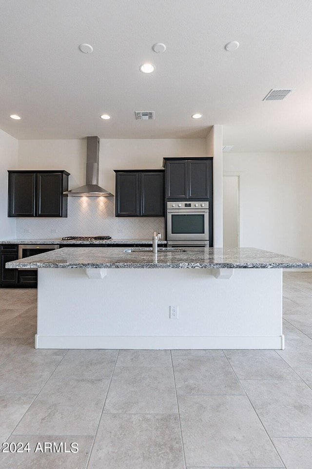 kitchen featuring light stone counters, a spacious island, sink, wall chimney range hood, and stainless steel gas stovetop