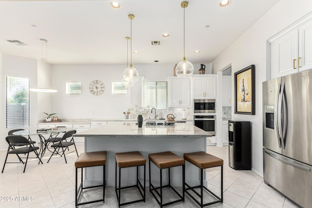 kitchen with a kitchen island with sink, light stone counters, stainless steel appliances, and white cabinets