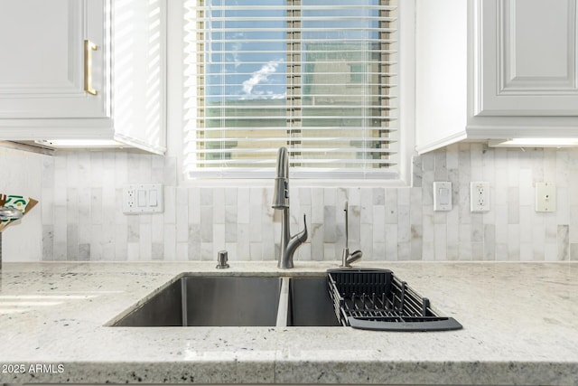 kitchen with light stone counters, backsplash, white cabinetry, and sink