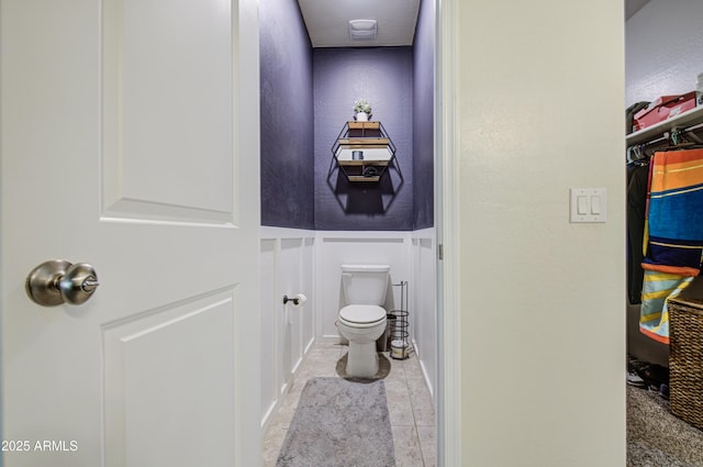 10856 E Primrose Ct, Florence, AZ 85132 - bathroom with a decorative wall, a spacious closet, tile patterned flooring, a wainscoted wall, and toilet