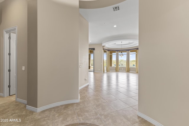 corridor with light tile patterned floors and a tray ceiling