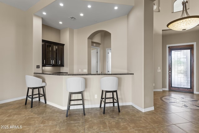 kitchen featuring a breakfast bar, hanging light fixtures, kitchen peninsula, dark stone countertops, and dark brown cabinets