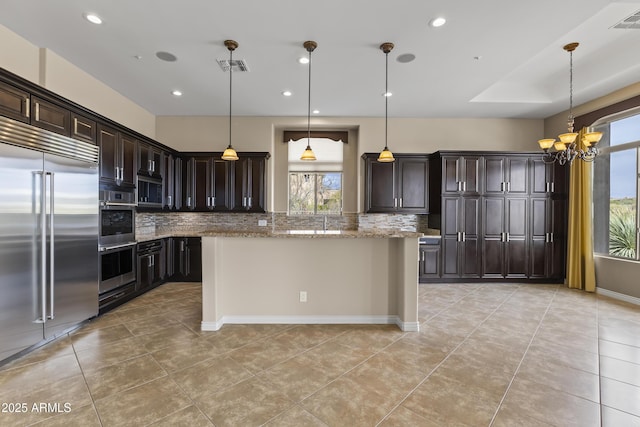 kitchen featuring light stone countertops, backsplash, dark brown cabinetry, stainless steel appliances, and hanging light fixtures