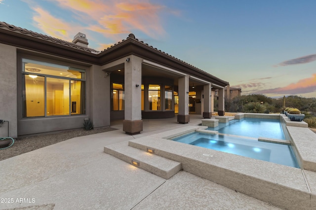 pool at dusk with a patio area and an in ground hot tub